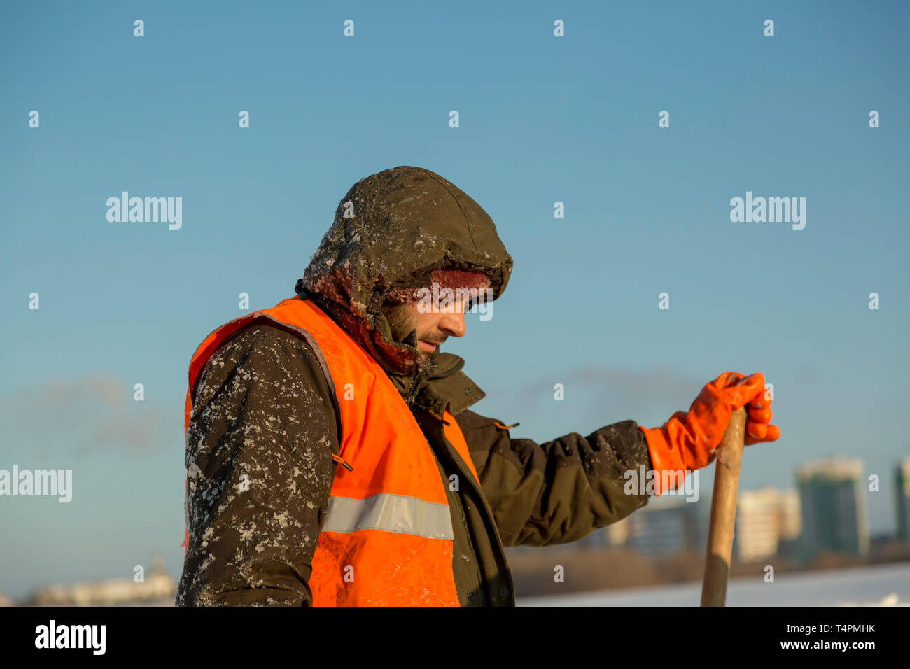 Lavoratore in un arancione giubbotto in profilo con un piano medio con la pala in mano Foto Stock