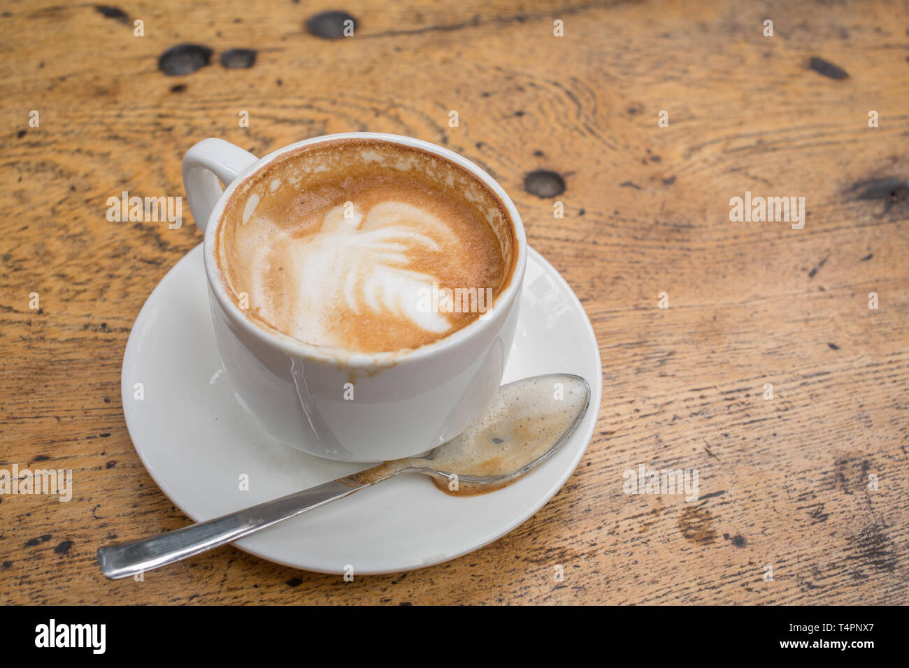 Una tazza di latte in una tazza con un cucchiaio su una tavola in legno rustico Foto Stock