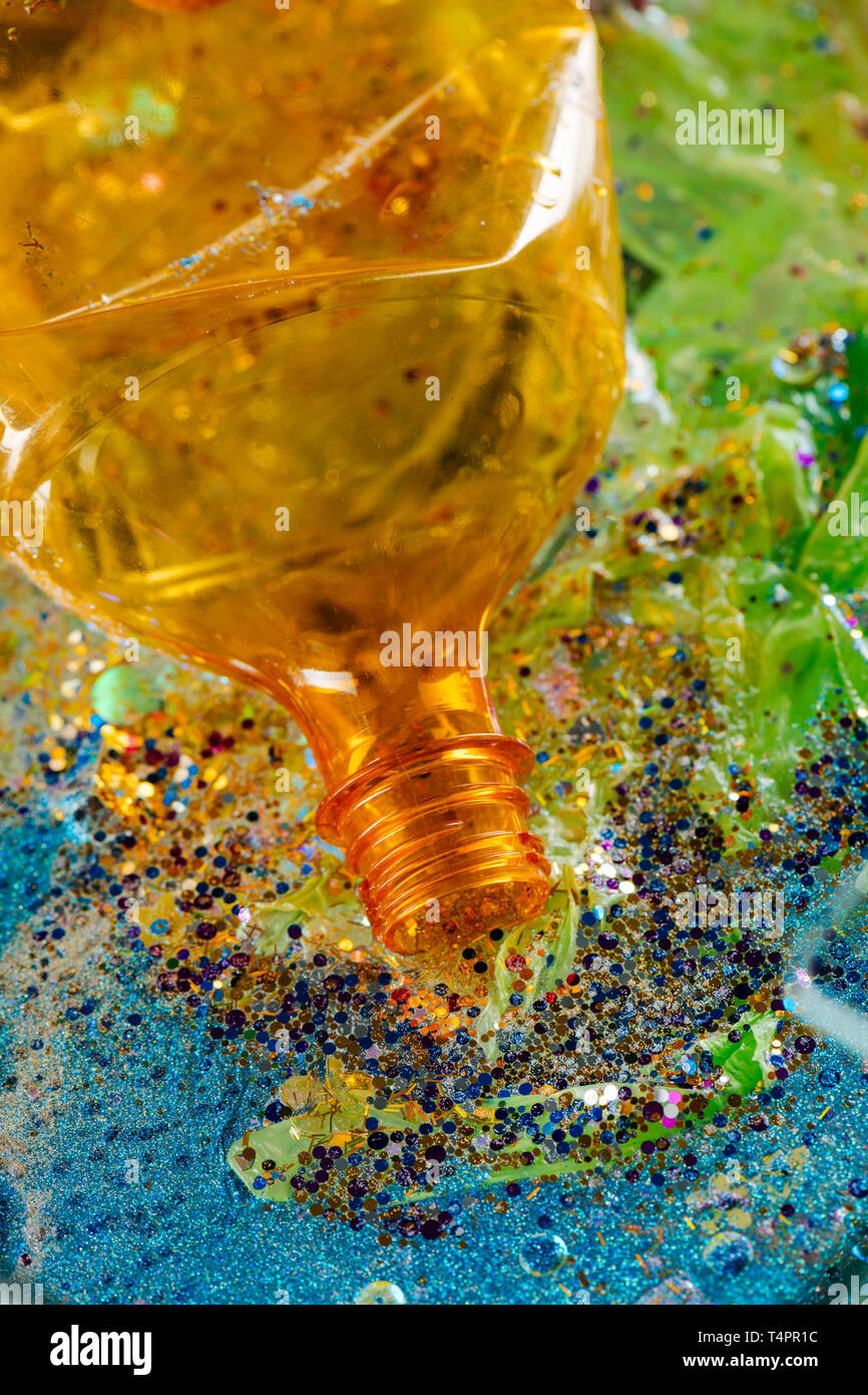 Giacente nel cestino. Orange ha aperto la bottiglia non fatti di plastica decomposto essendo circondato con glitter pezzi Foto Stock