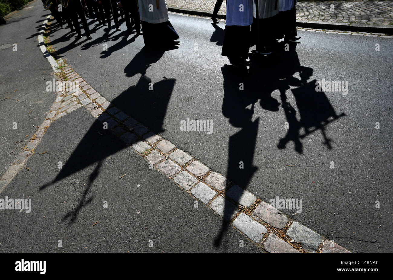 Lohr am Main, Germania. Xix Apr, 2019. Le ombre dei chierichetti che porta una croce e flags può essere visto sul terreno durante una processione del Venerdì santo. Tredici life-size figure raffiguranti scene della Passione di Cristo sono trasportate attraverso la città nella tradizionale processione. Credito: Karl-Josef Hildenbrand/dpa/Alamy Live News Foto Stock