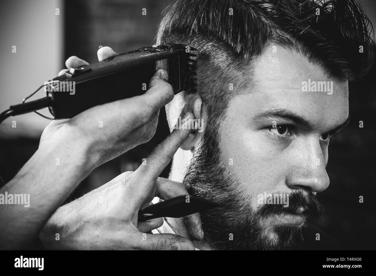 Giovani bel barbiere rendendo haircut per attraente uomo barbuto al barbiere. Nero e bianco o incolore foto. Acconciatura, salone di bellezza e parrucchiere, barbiere, il concetto di stile di vita. Caucasian modelli maschili. Foto Stock