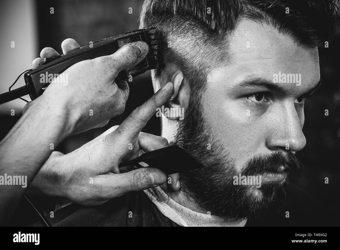 Giovani bel barbiere rendendo haircut per attraente uomo barbuto al barbiere. Nero e bianco o incolore foto. Acconciatura, salone di bellezza e parrucchiere, barbiere, il concetto di stile di vita. Caucasian modelli maschili. Foto Stock
