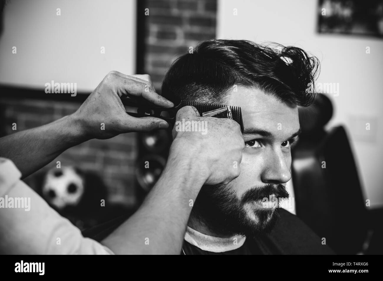Giovani bel barbiere rendendo haircut per attraente uomo barbuto al barbiere. Nero e bianco o incolore foto. Acconciatura, salone di bellezza e parrucchiere, barbiere, il concetto di stile di vita. Caucasian modelli maschili. Foto Stock