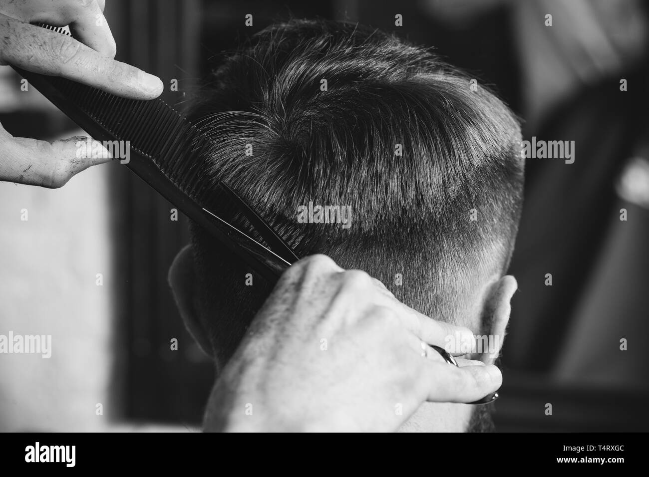 Giovani bel barbiere rendendo haircut per attraente uomo barbuto al barbiere. Nero e bianco o incolore foto. Acconciatura, salone di bellezza e parrucchiere, barbiere, il concetto di stile di vita. Caucasian modelli maschili. Foto Stock