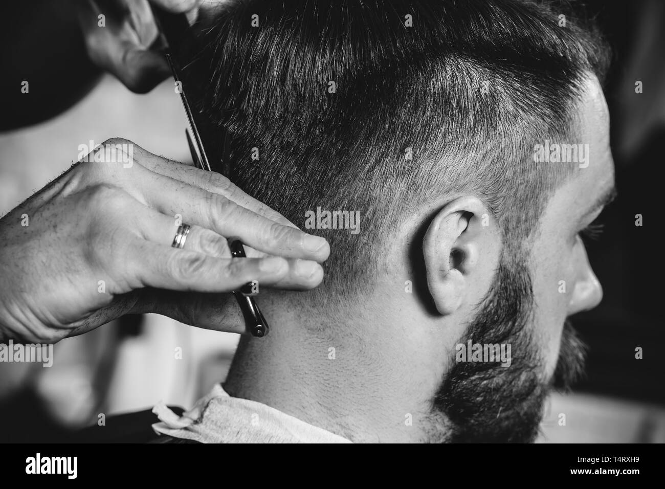 Giovani bel barbiere rendendo haircut per attraente uomo barbuto al barbiere. Nero e bianco o incolore foto. Acconciatura, salone di bellezza e parrucchiere, barbiere, il concetto di stile di vita. Caucasian modelli maschili. Foto Stock