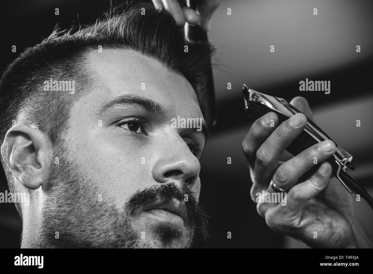 Giovani bel barbiere rendendo haircut per attraente uomo barbuto al barbiere. Nero e bianco o incolore foto. Acconciatura, salone di bellezza e parrucchiere, barbiere, il concetto di stile di vita. Caucasian modelli maschili. Foto Stock