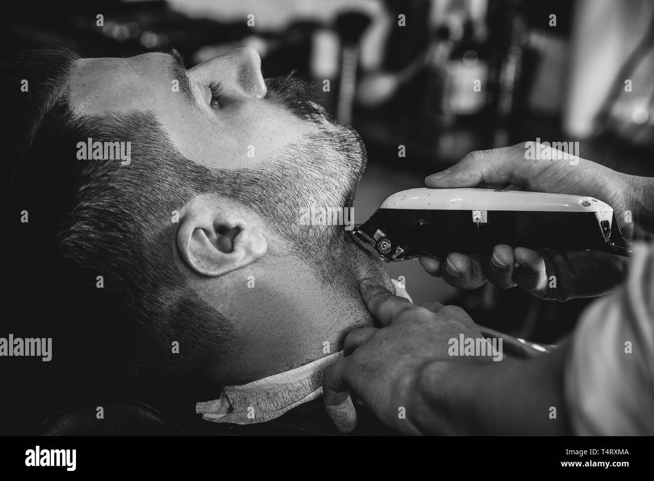 Client durante la rasatura della barba in barberia. Giovani bel barbiere e attraente uomo barbuto. Nero e bianco o incolore foto. Acconciatura, salone di bellezza e parrucchiere, barbiere, il concetto di stile di vita. Caucasian modelli maschili. Foto Stock