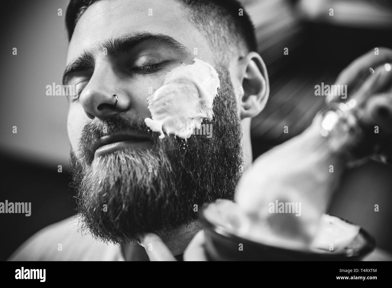 Client durante la rasatura della barba in barberia. Barbiere femmina al salone. La parità tra i sessi. Donna nel maschio professione. Nero e bianco o incolore foto. Acconciatura, salone di bellezza e parrucchiere, il concetto di stile di vita. Foto Stock