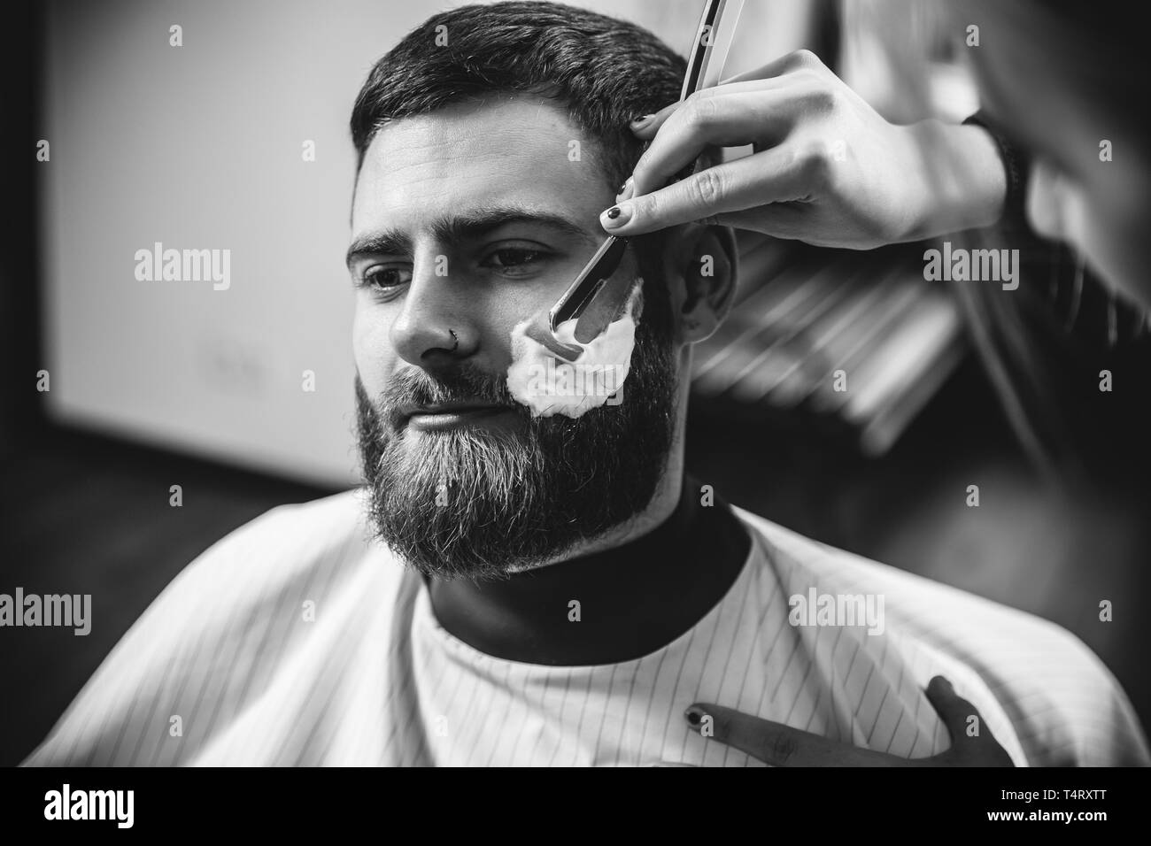 Client durante la rasatura della barba in barberia. Barbiere femmina al salone. La parità tra i sessi. Donna nel maschio professione. Nero e bianco o incolore foto. Acconciatura, salone di bellezza e parrucchiere, il concetto di stile di vita. Foto Stock