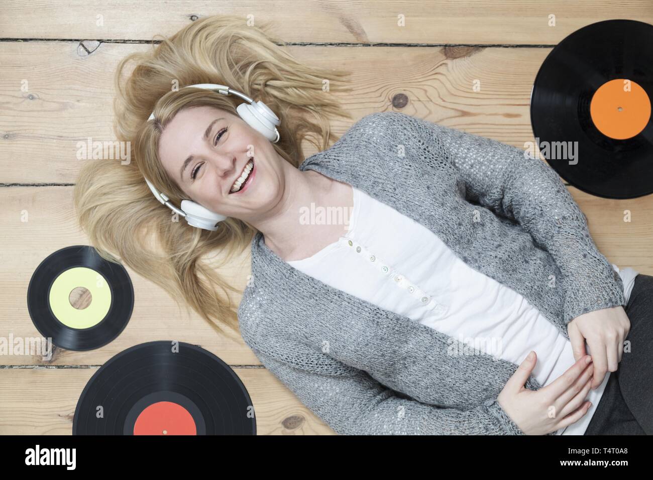 Giovane donna bionda sdraiato sul pavimento di legno, circondato da record Foto Stock Giovane donna bionda sdraiato sul pavimento di legno, circondato da record Foto Stock