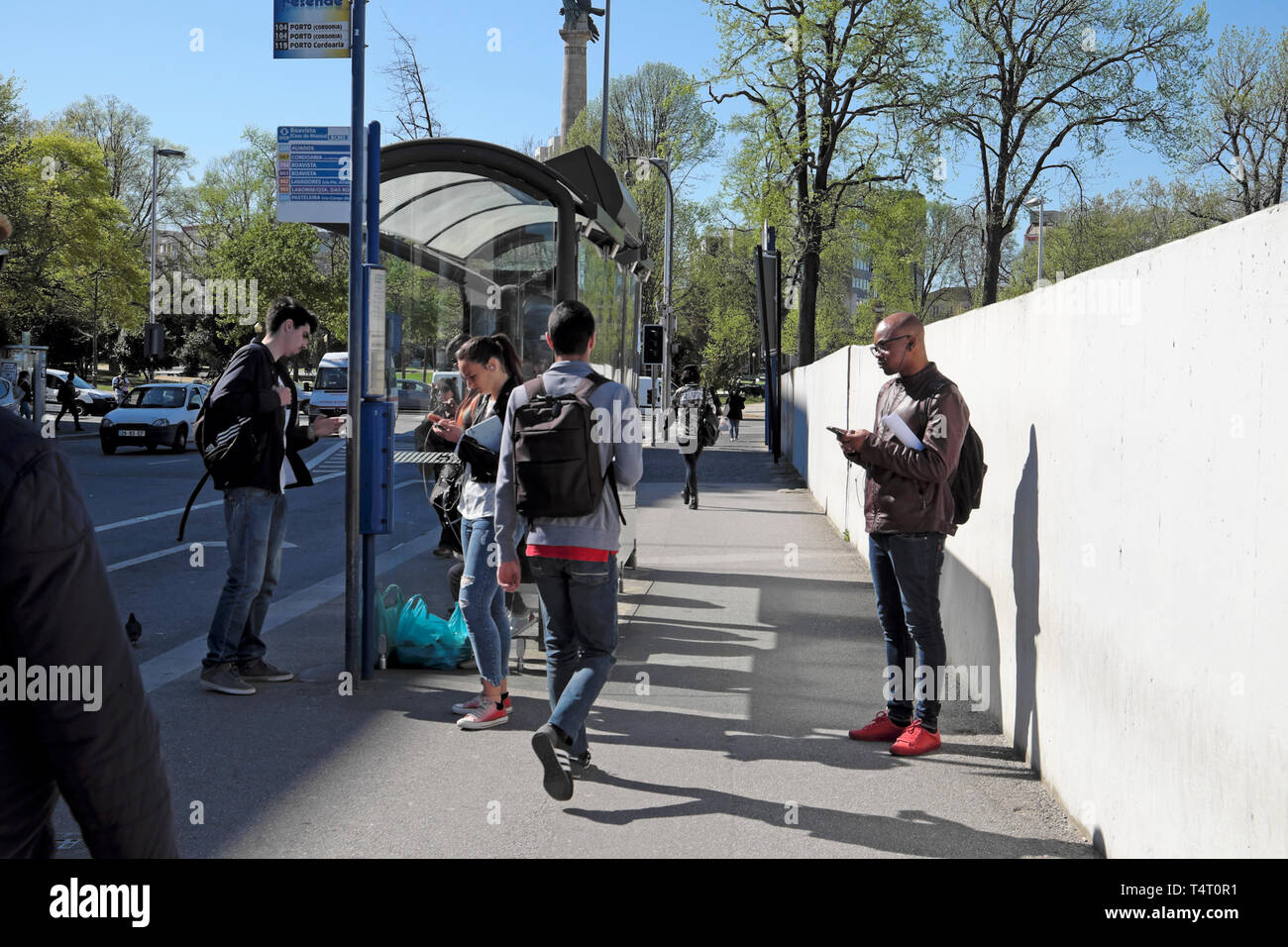 Persone scrivere messaggi su telefoni cellulari in attesa sulla strada per il trasporto in autobus shelter in primavera nella città di Porto Portogallo Europa KATHY DEWITT Foto Stock
