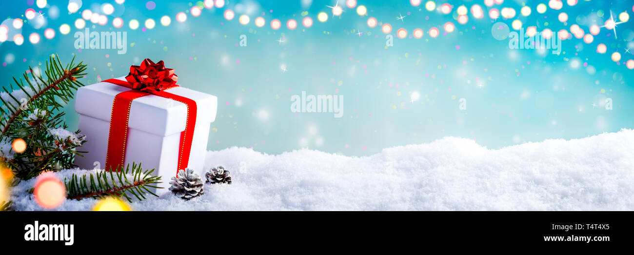 Regalo di natale Scatola, rami di abete e pino coni, sulla neve con le luci di Natale Foto Stock