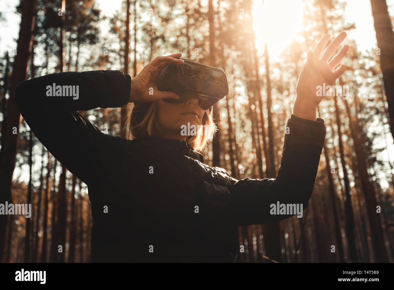 La donna nella foresta con la realtà virtuale auricolare guardando dritto e cercando di toccare qualcosa con la mano Foto Stock