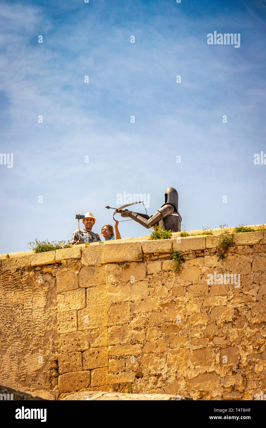 Giovane prendere selfie con bastone con acciaio scultura medievale di archer contro il cielo blu al di sopra del Castello di Santa Barbara, Alicante Spagna Foto Stock