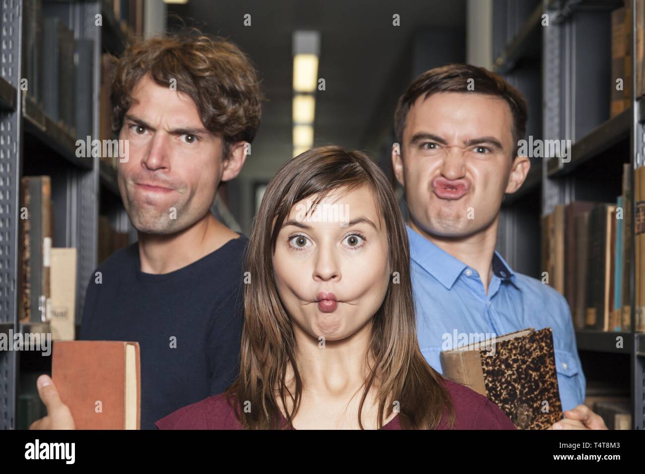 Tre studenti in biblioteca grimace di trazione Foto Stock
