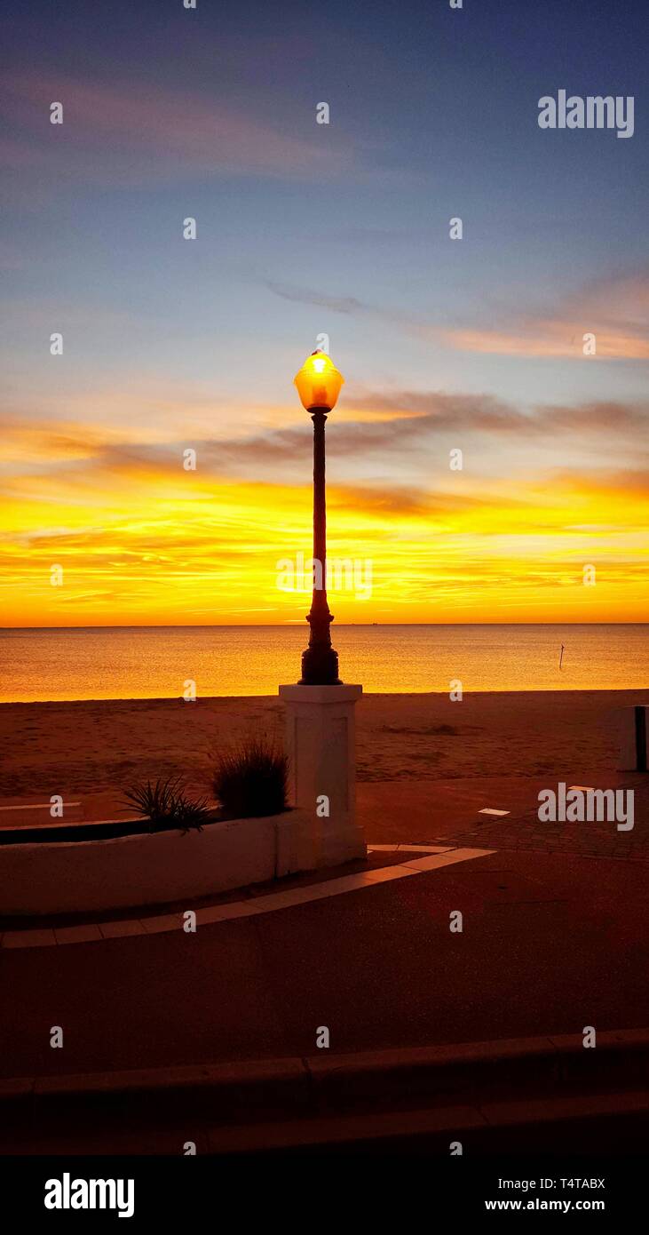 Lampione acceso sul bordo della spiaggia al tramonto Foto Stock