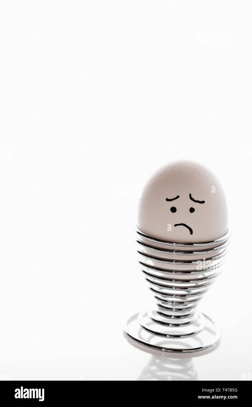 Singola bianca, anthropomorph uovo di pollo in uovo silver cup con triste espressione facciale. Foto Stock