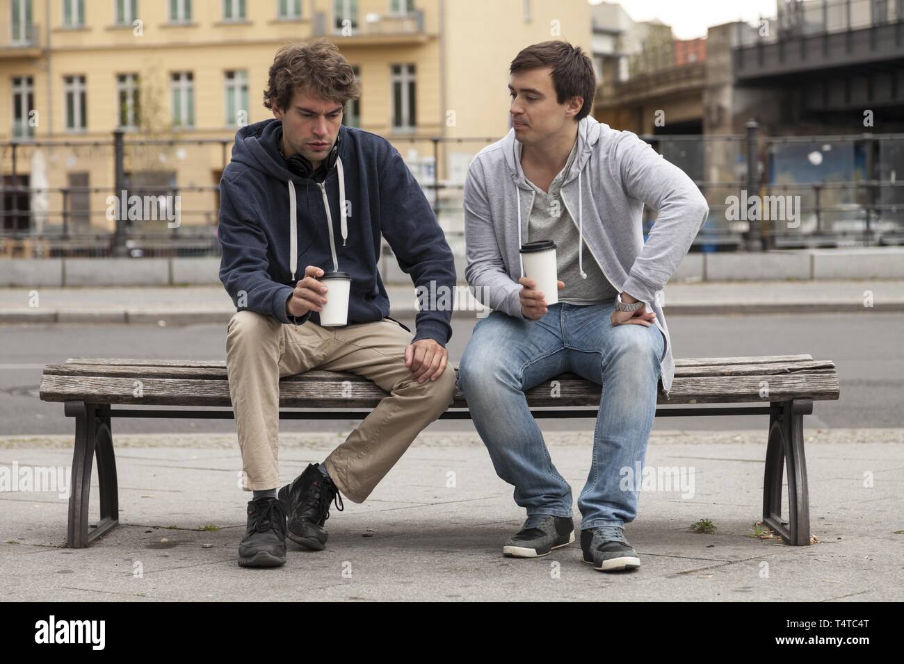 Giovani uomini seduti su una panchina e bere il caffè Foto Stock