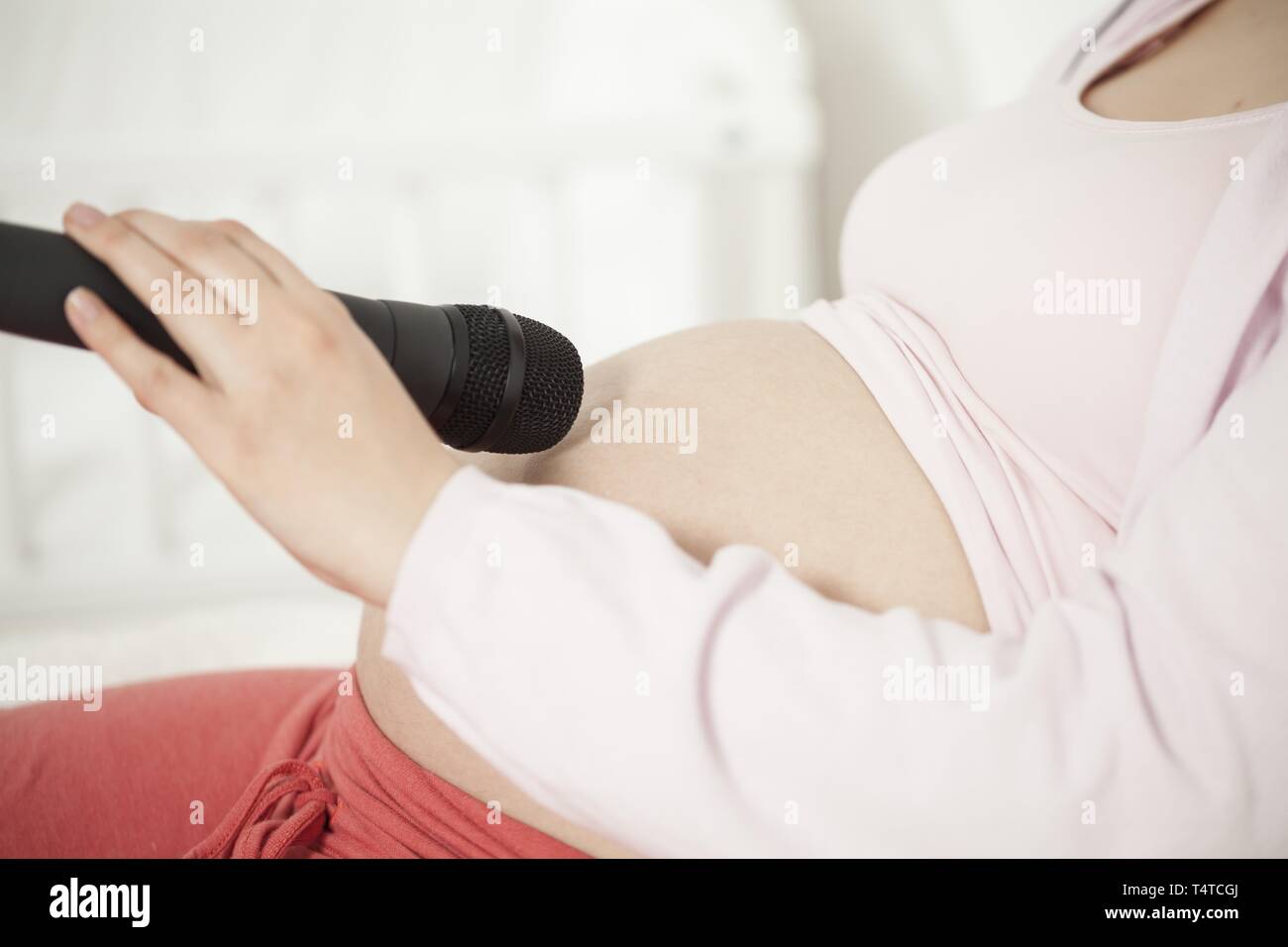 Donna incinta holding micrphone sulla pancia Foto Stock