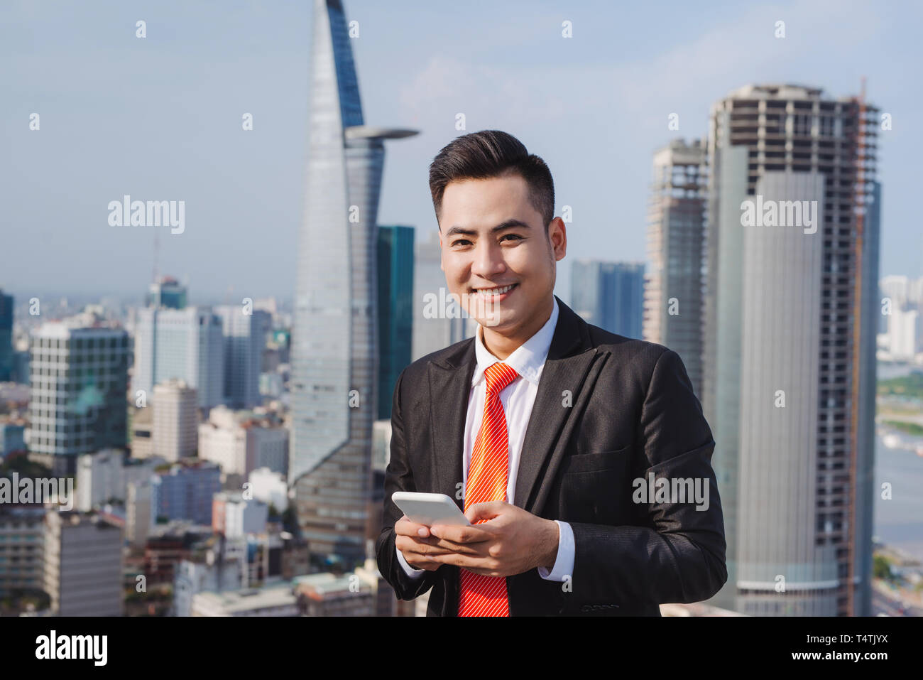 Imprenditore tramite telefono mobile app texting al di fuori dell'ufficio in città urbana con grattacieli edifici in background. Giovane uomo caucasico holding s Foto Stock