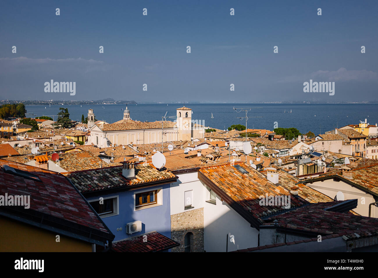 Vista sui tetti di tegole rosse del piccolo paese sotto il bellissimo cielo al tramonto in autunno a Garda, Italia. Tetti di tradizionali case italiane. Foto Stock