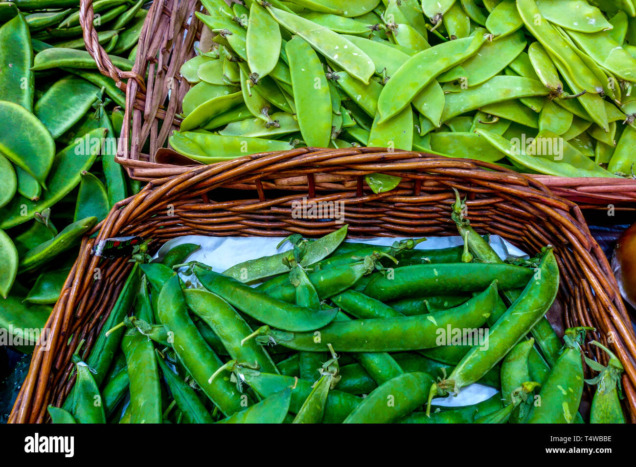 Cialde di piselli freschi in cesto presso il mercato agricolo, piante leguminose Foto Stock