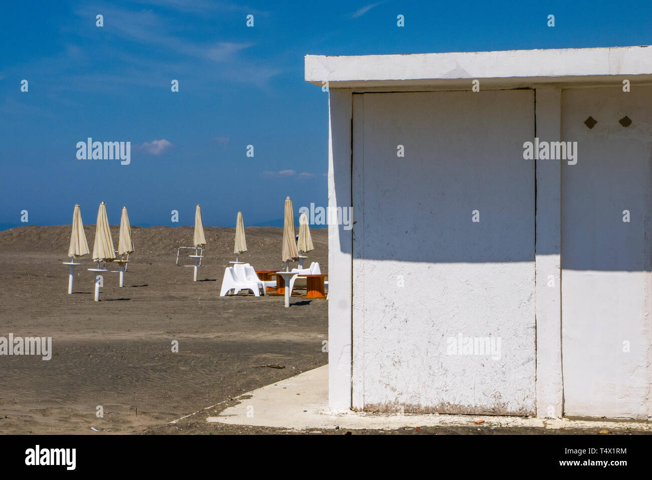 Bianco cabina balneare e ombrelloni bianchi su una spiaggia deserta, nel mese di aprile con il blu del cielo in background Foto Stock