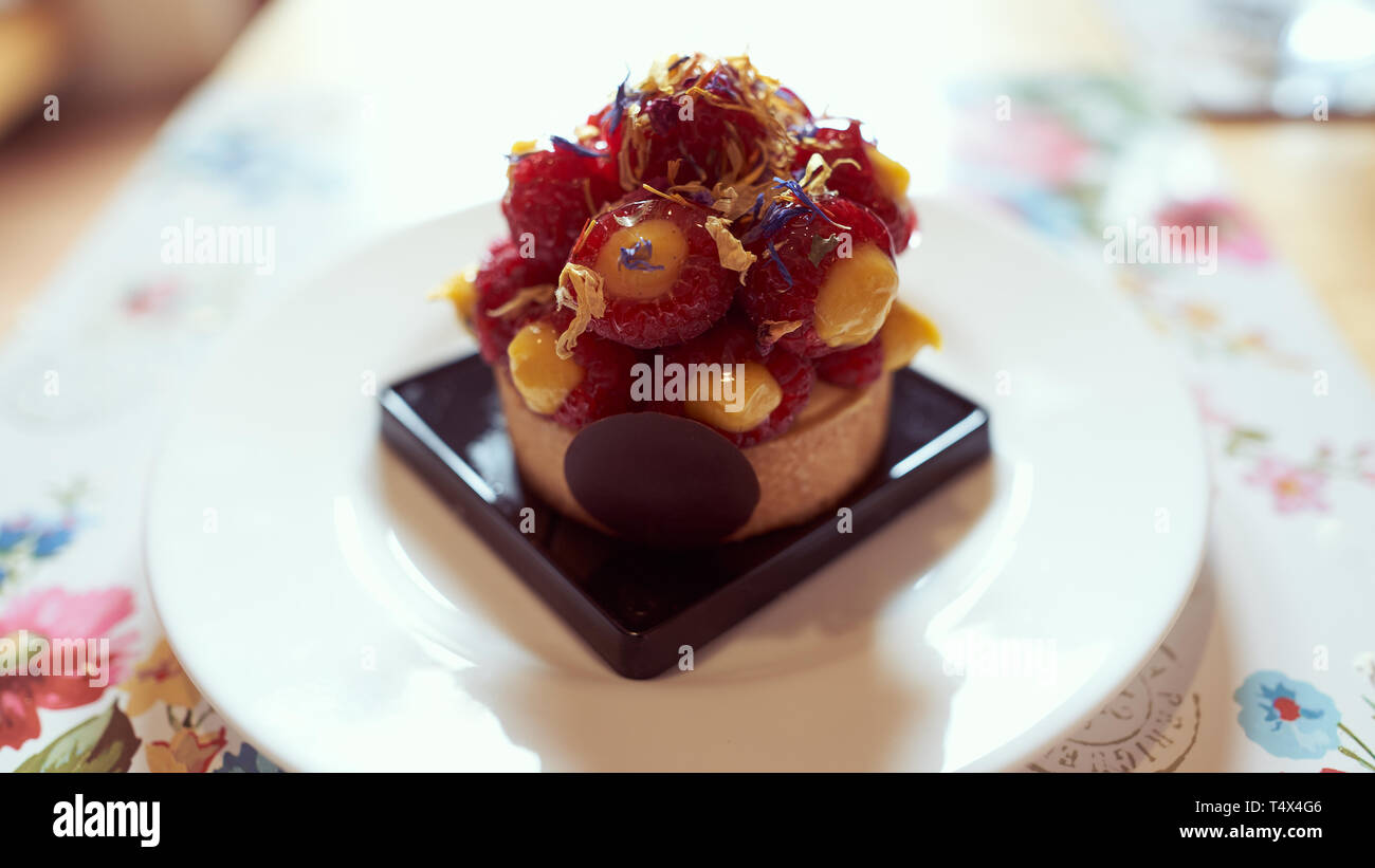 Frutta italiana di sfoglia con crema pasticcera, lamponi e delicati petali di fiore, servita su una porcellana bianca la piastra al di sopra di un cartellone con motivi floreali Foto Stock