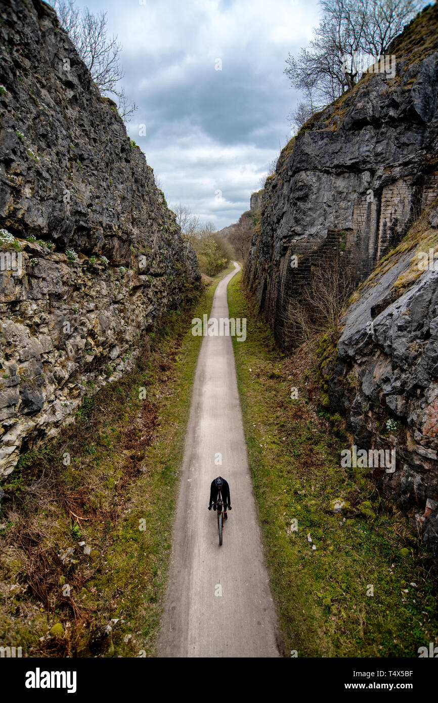 Un uomo che cavalca una bicicletta attraverso un taglio lungo il sentiero Monsal nel Derbyshire Peak District. Foto Stock