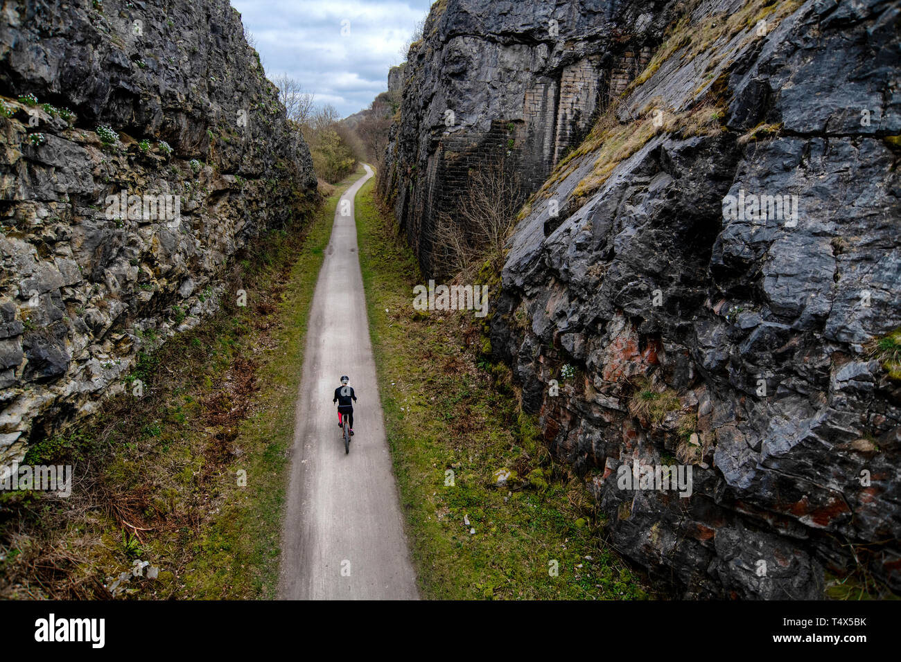 Un uomo che cavalca una bicicletta attraverso un taglio lungo il sentiero Monsal nel Derbyshire Peak District. Foto Stock