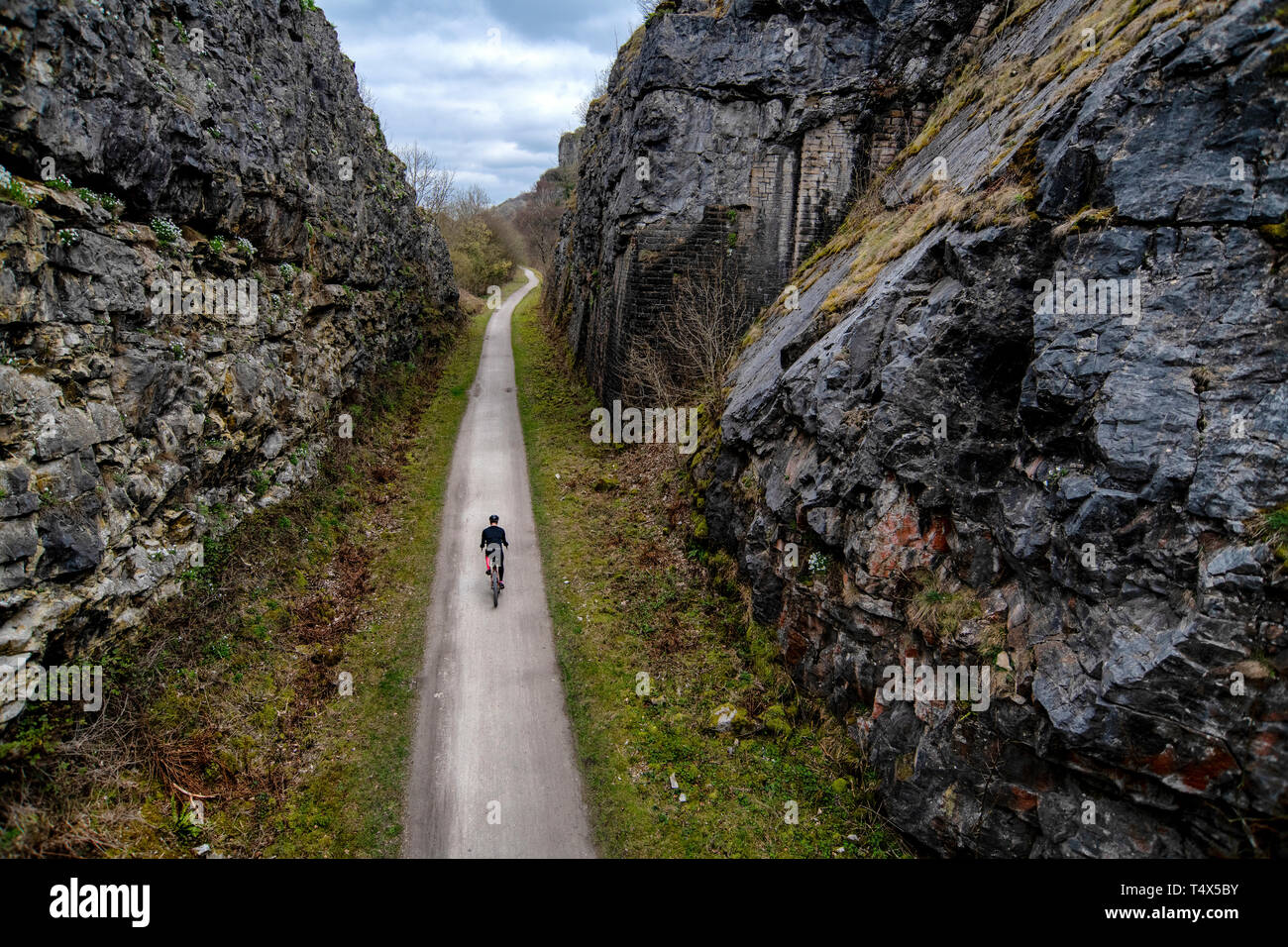 Un uomo che cavalca una bicicletta attraverso un taglio lungo il sentiero Monsal nel Derbyshire Peak District. Foto Stock