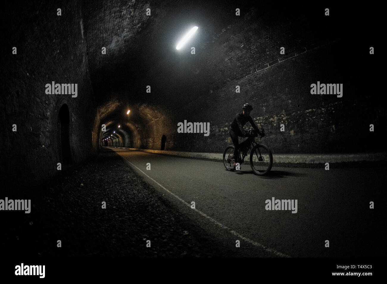 Un uomo che cavalca una bicicletta attraverso un tunnel lungo il sentiero Monsal nel Derbyshire Peak District. Foto Stock