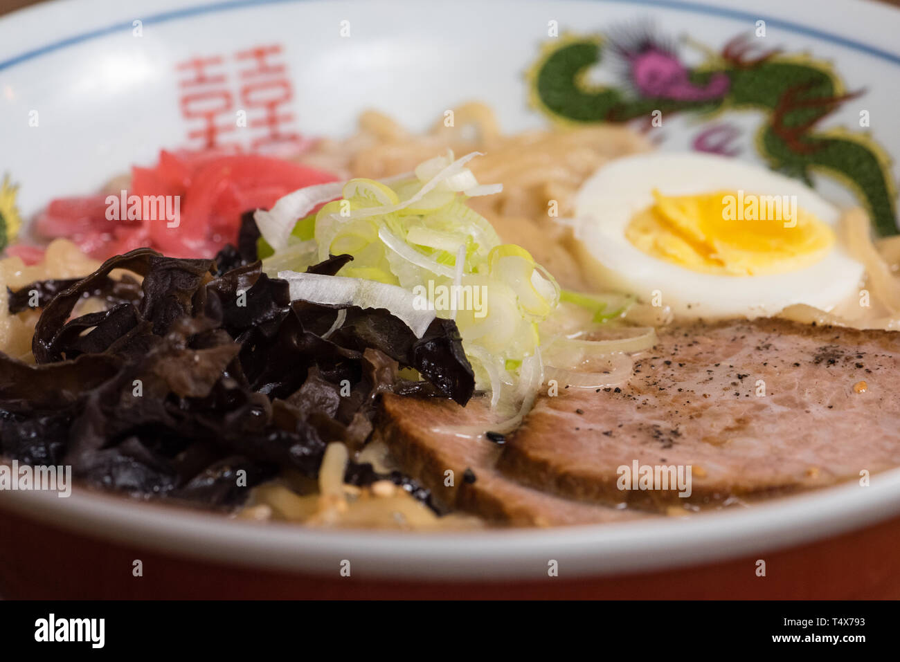 Ramen tonkotsu con carne di maiale, latte di soia, brodo di carne di maiale, funghi neri, uova, cipolle, servita in una ciotola di legno scuro dello sfondo della tabella Foto Stock