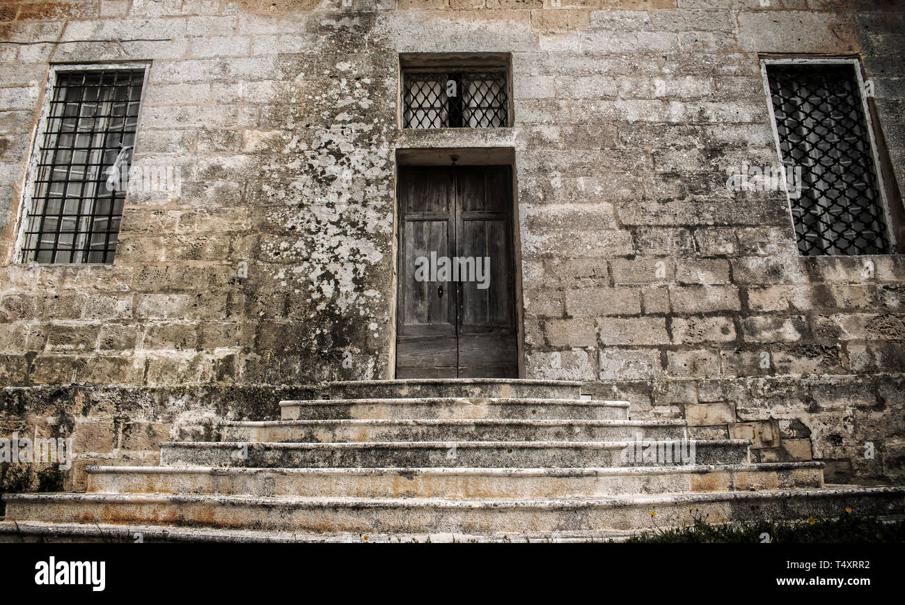 La vecchia porta nella parete di roccia calcarea. Una vecchia porta di legno e due finestre di ferro all'interno di una tipica pietra calcarea maltese parete. Foto Stock