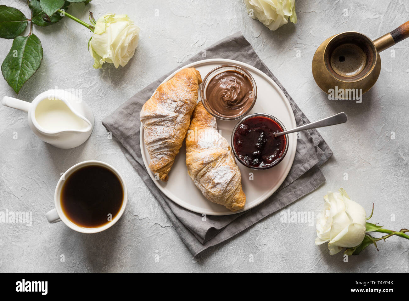 Concetto prima colazione francese. Tazza di caffè, romantica Bianca Rose e i croissant appena sfornati. Vista dall'alto. Foto Stock