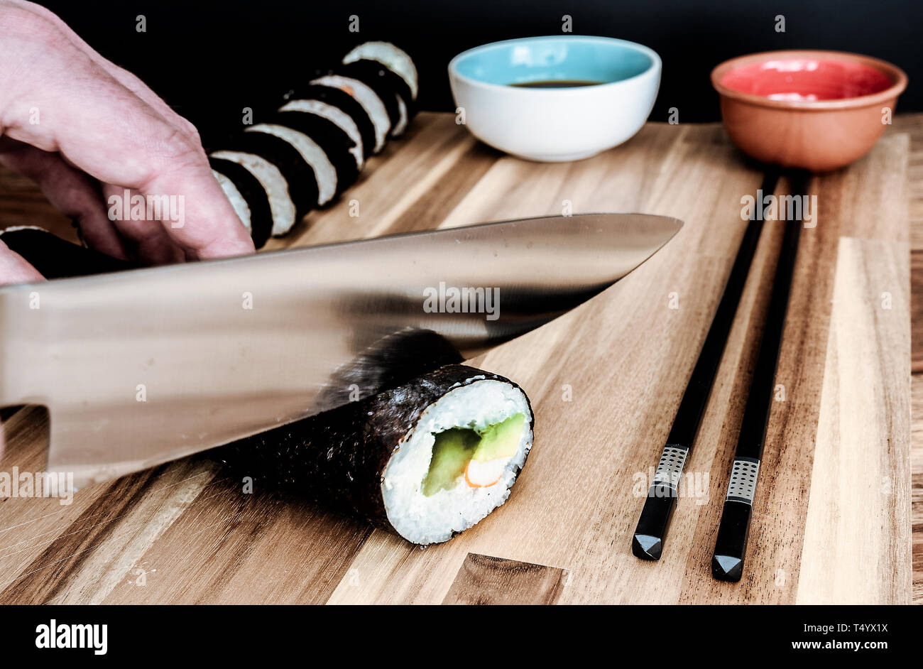 Close-up di persona in casa il taglio di rotoli di sushi con coltello da cucina Foto Stock