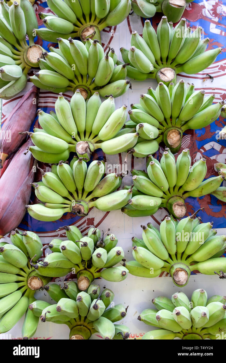 Molti banana acerba gettare sul tavolo per vendere, verticale Foto Stock