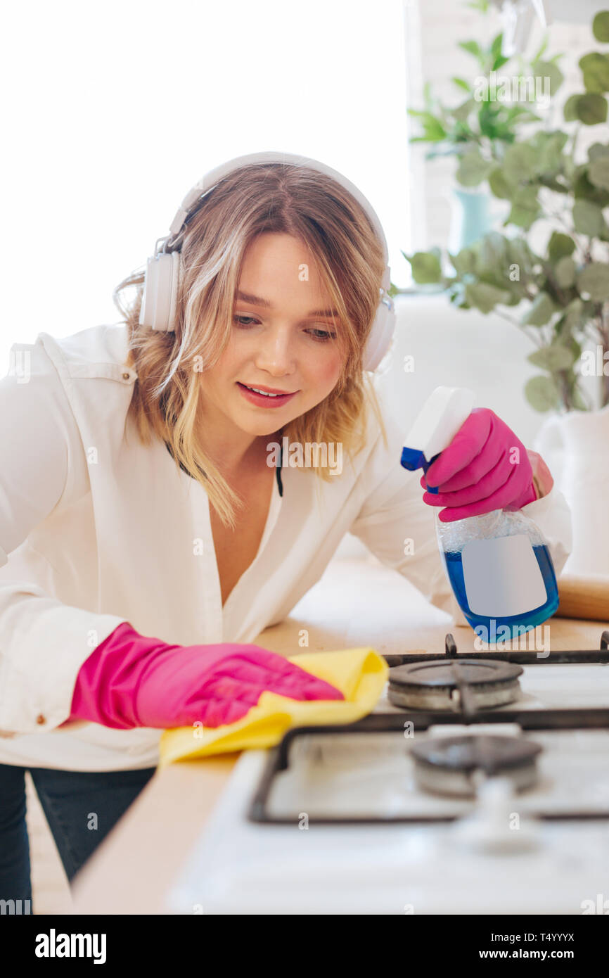 Amore per la pulizia. Positivo giovane donna usando un agente detergente durante la pulizia del fornello a gas Foto Stock
