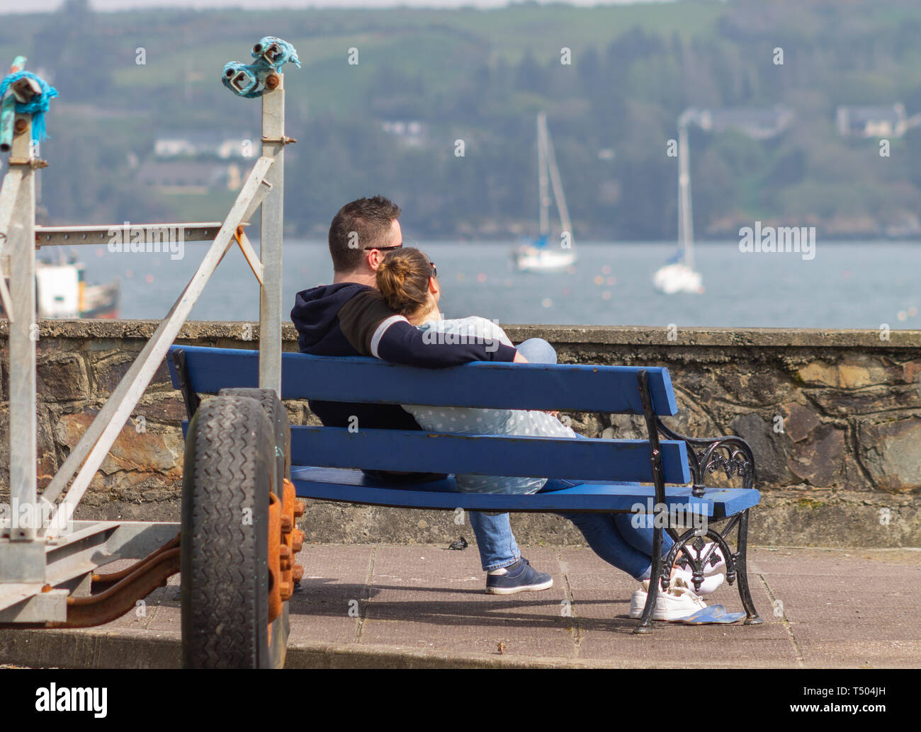 Coppia giovane seduto su una panchina nel parco del mare a braccetto godendo di ogni altri company sotto il sole Foto Stock