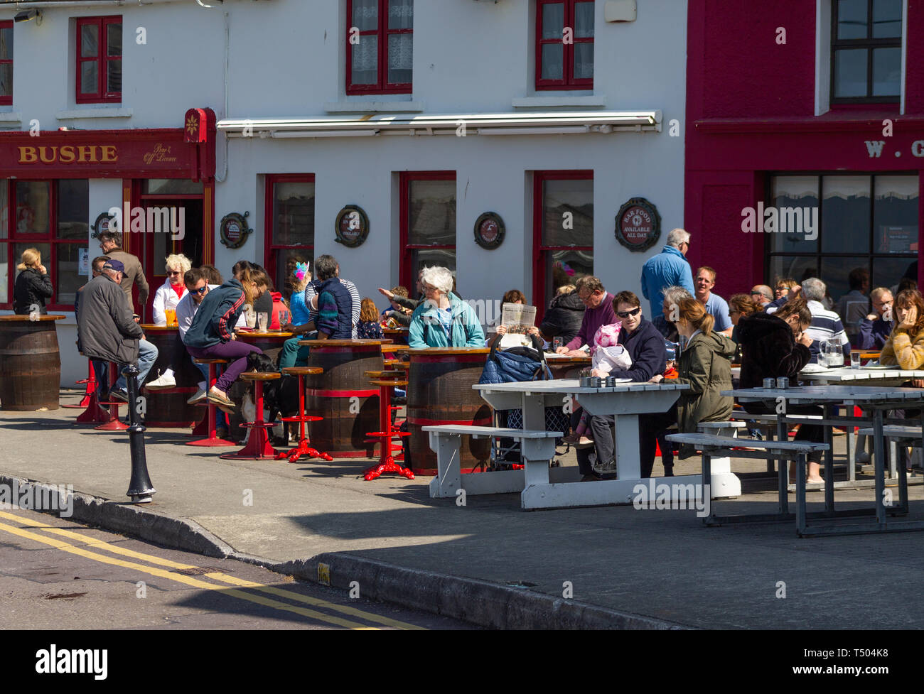 La folla di gente seduta al di fuori di un pub, bar sotto il sole godendo il pranzo e bersi un drink. Baltimore Irlanda Foto Stock