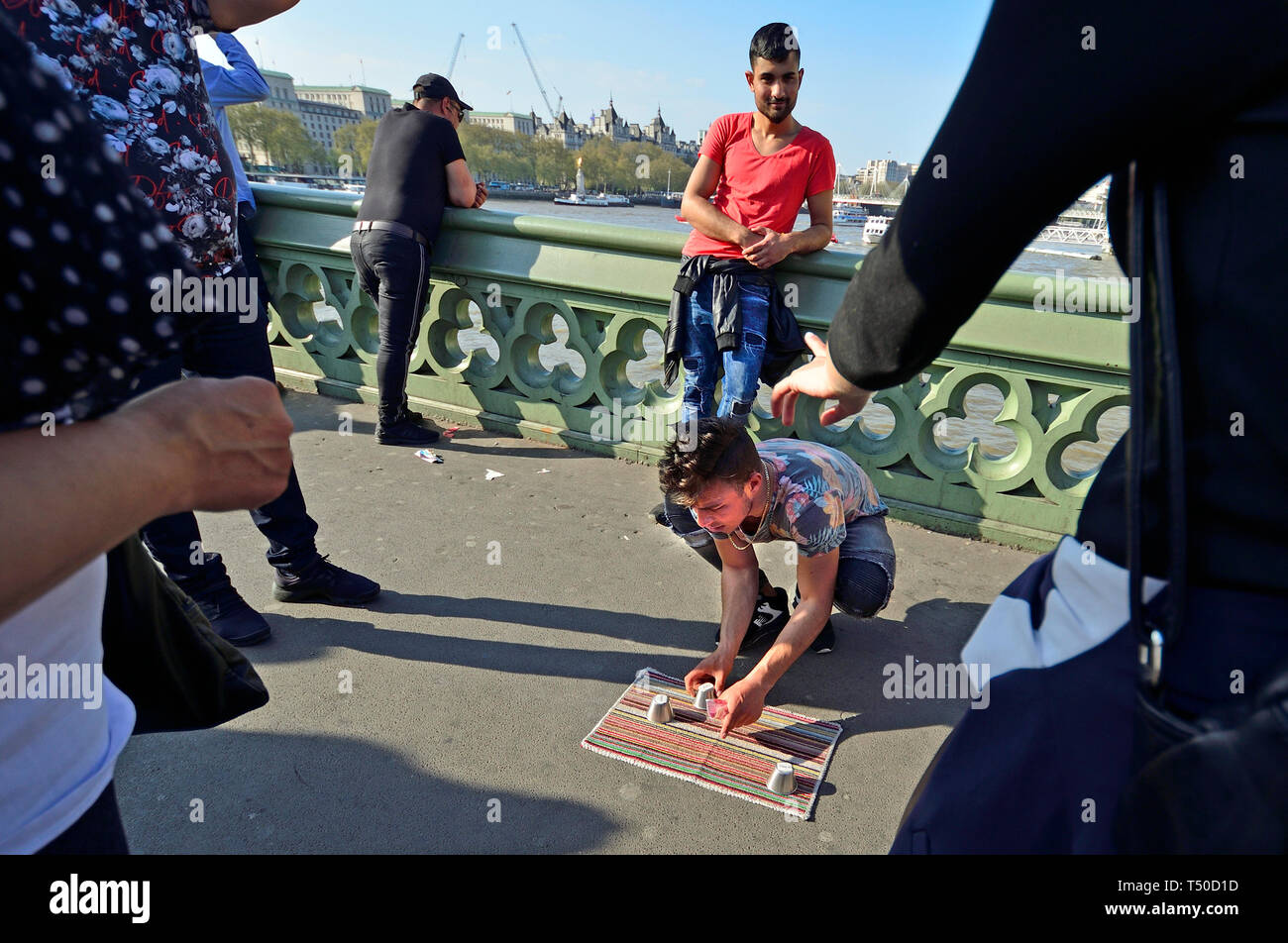 Londra, Regno Unito. 19 apr 2019. In una trafficata buon venerdì festivo della pavimentazione di Westminster Bridge è quasi bloccato da più di 10 giochi illegali delle 3 tazze di trucco o coppa e la sfera, progettato per alleviare i turisti dei loro soldi avendo stooges apparentemente vincere grandi somme per primo. Credito: PjrFoto/Alamy Live News Foto Stock