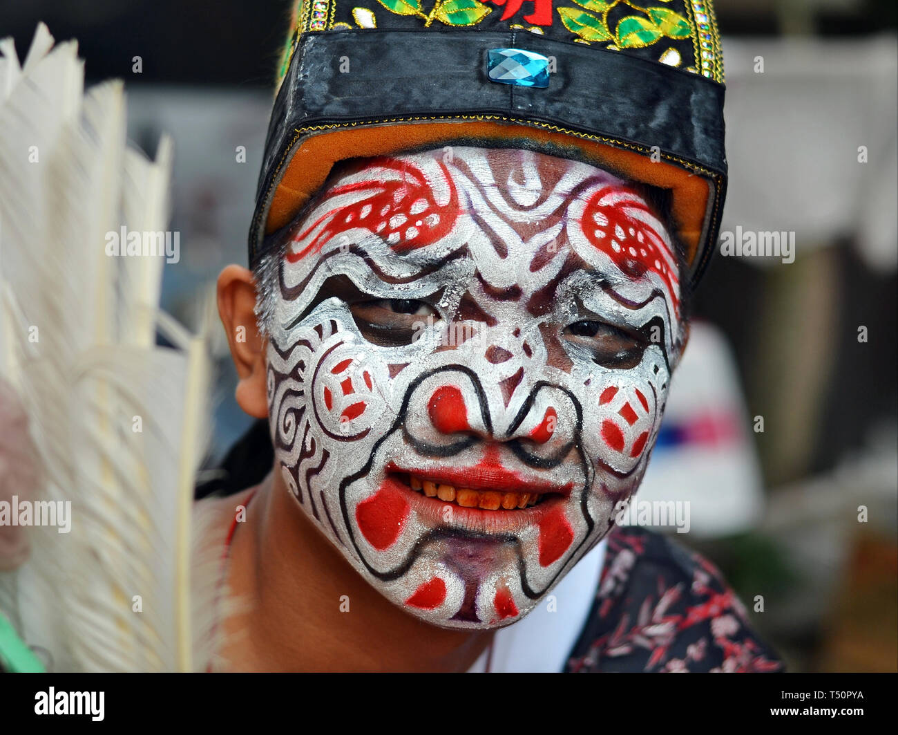 Betelnut-masticare giovane uomo di Taiwan con il rosso-denti macchiati (street interprete di una troupe zhentou) ha il suo volto dipinto con una elaborata maschera facciale. Foto Stock