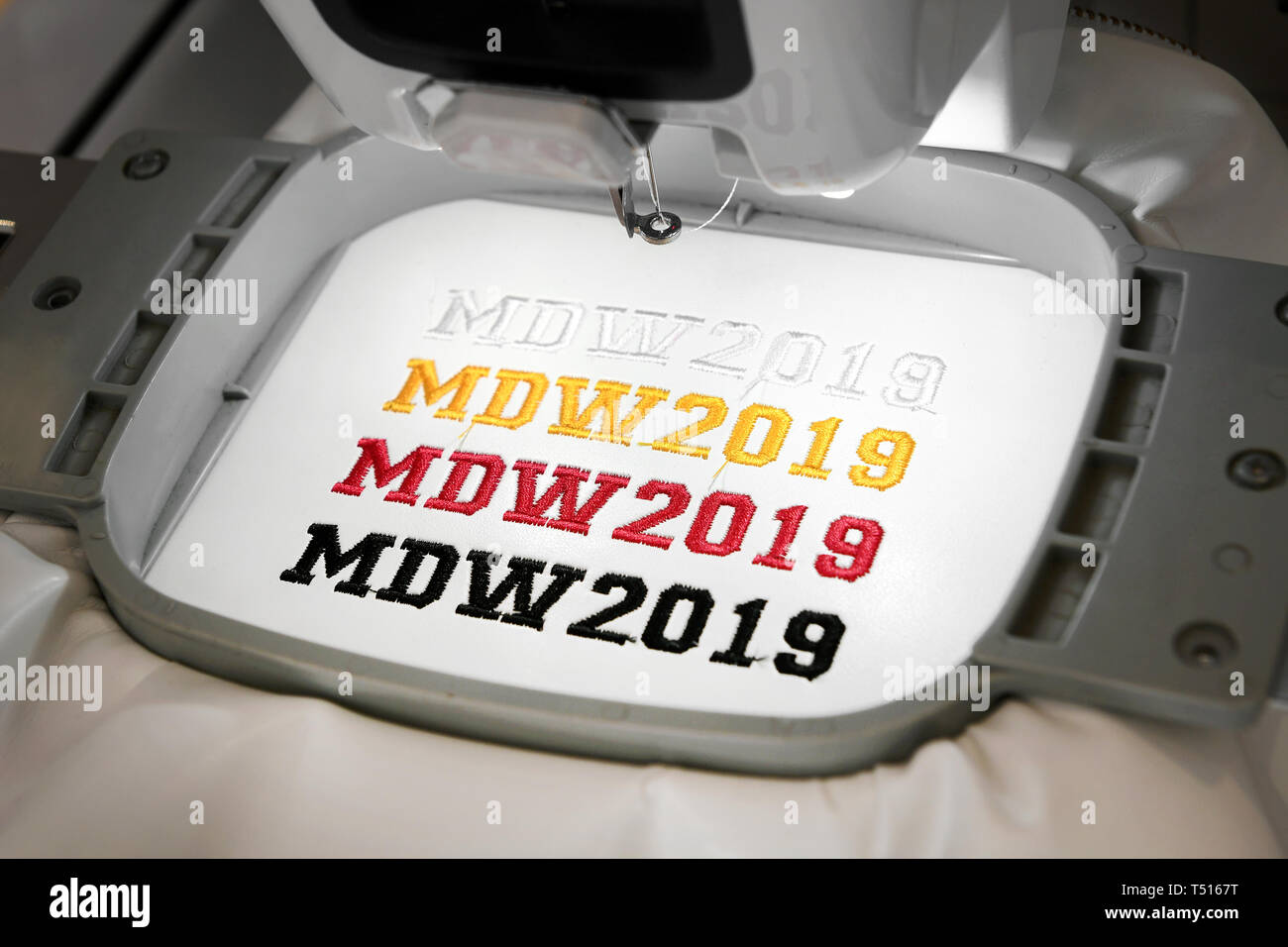 Macchina da ricamo automatica rendendo MDW 2019 segni di diversi colori su tessuto bianco, visualizzato in primo piano Foto Stock