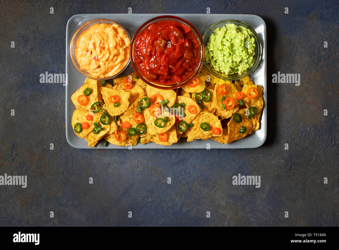 Messicano di mais giallo tortilla chips nachos con jalapeno, guacamole, la salsa al formaggio e salsa su sfondo blu scuro Foto Stock