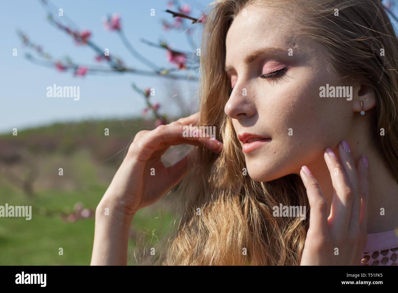 Bella donna bionda in un fiorito giardino di pesche in primavera con fiori di colore rosa Foto Stock