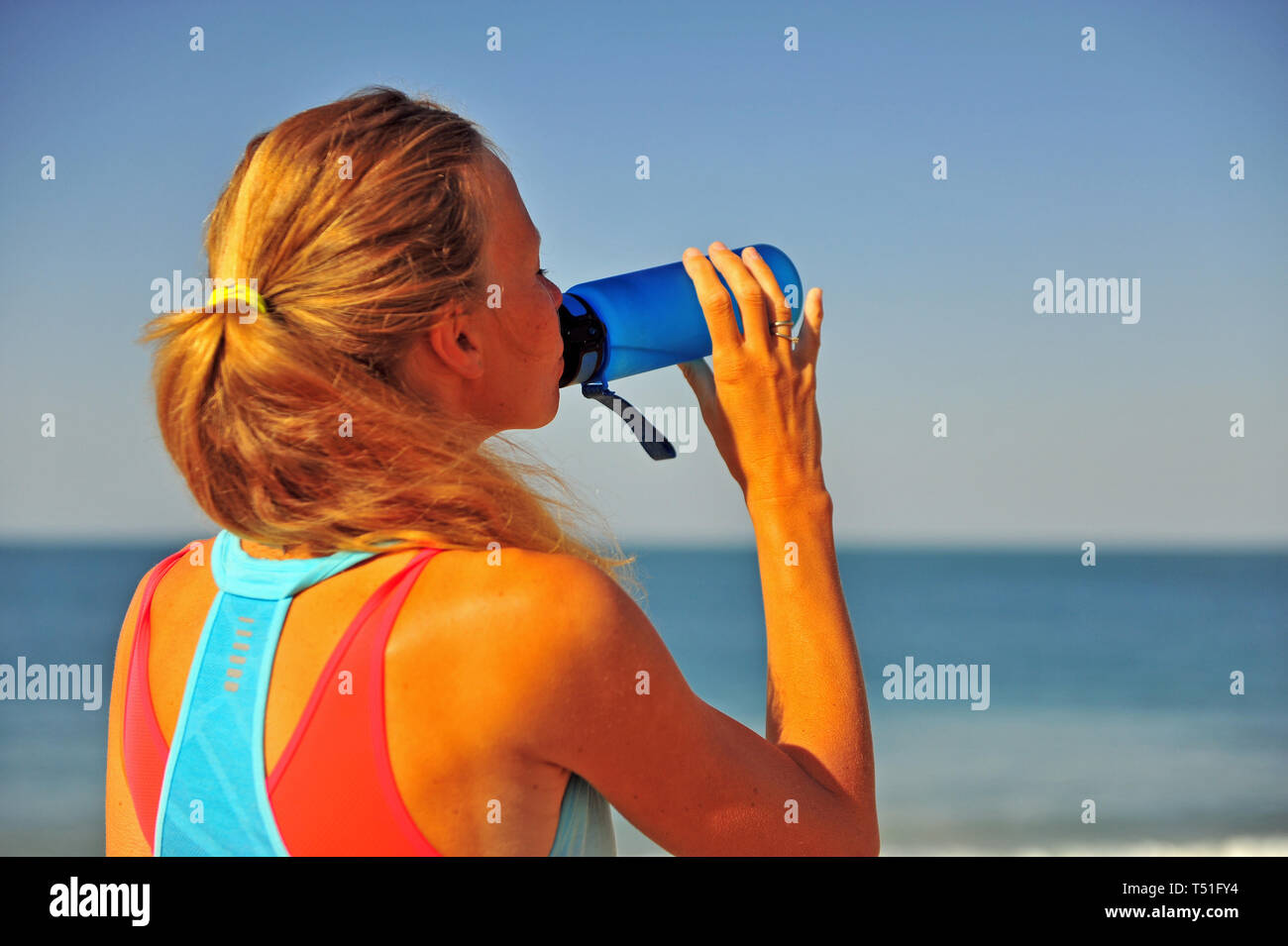 Abbracciare le Vibes costiere: Una giovane donna che fa jogging energico sulla spiaggia, immergersi nel sole, nella sabbia e nella serenità dell'aria aperta Foto Stock