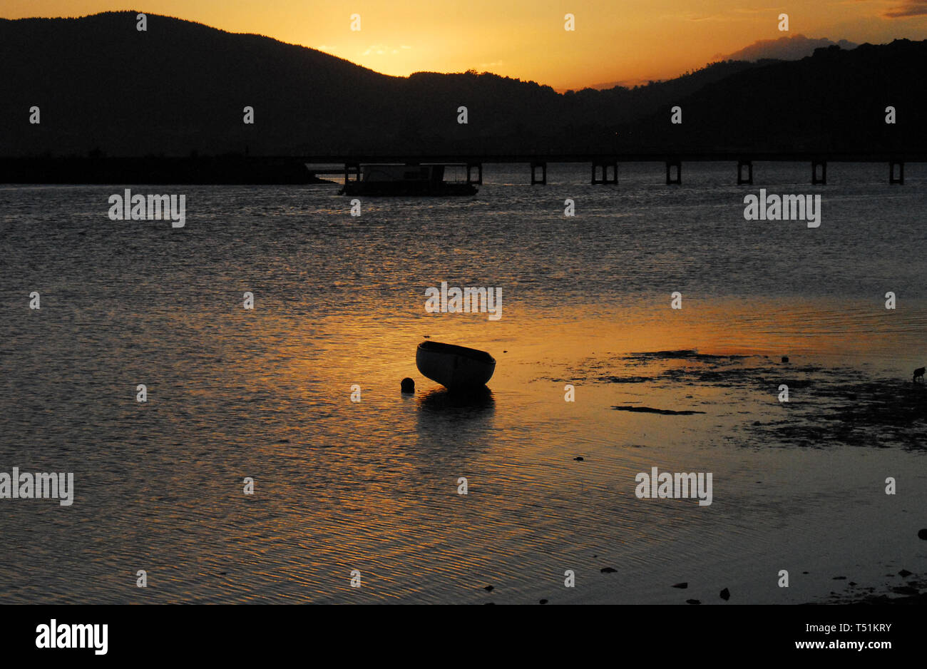 Una bellissima scena romantica di un grezzo antica barca da pesca riflessa nelle acque del tramonto di Knysna ingresso in Sud Africa. Foto Stock