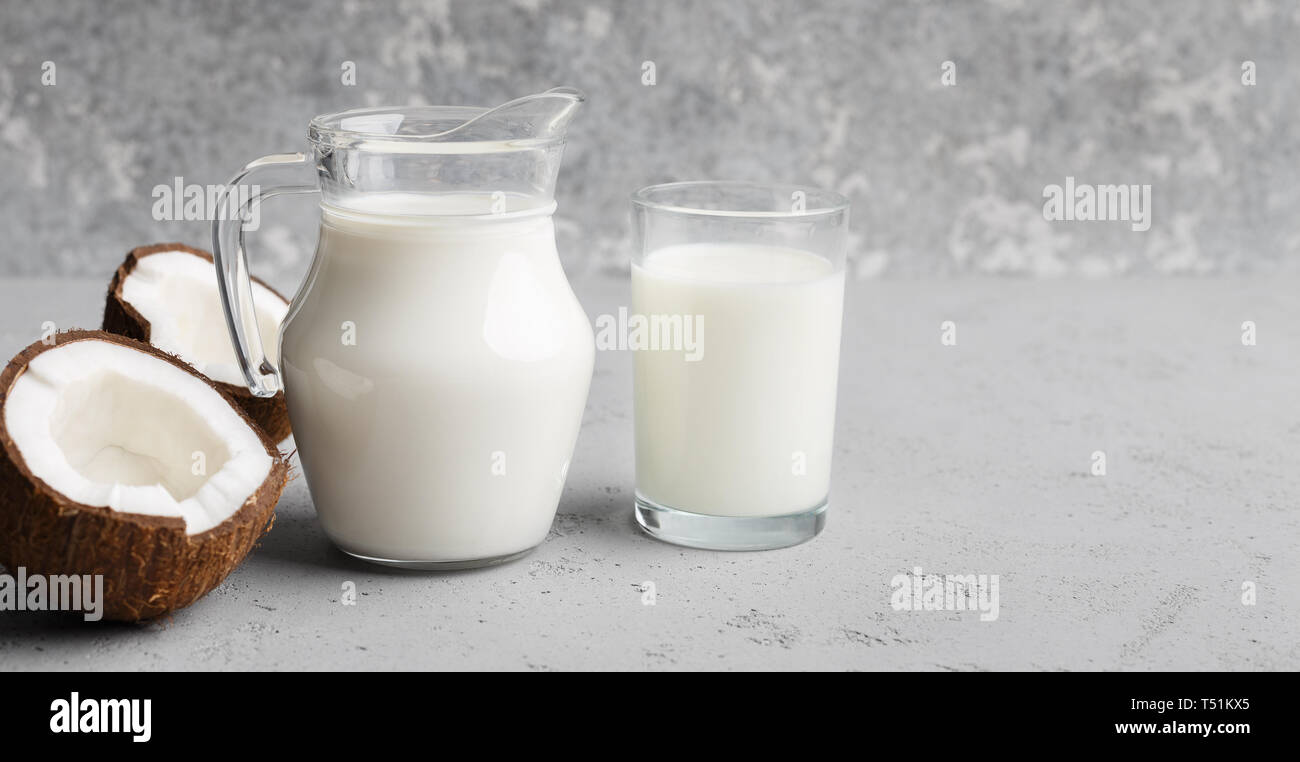 Un trito di cocco fresco e barattolo di latte di cocco su sfondo grigio. Organici di latte alternativi Foto Stock