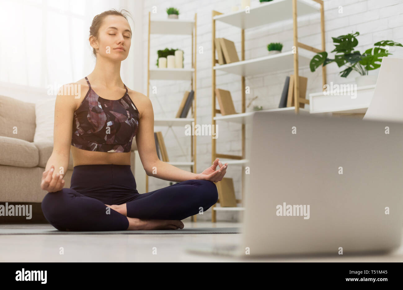 Meditando con il computer portatile. Donna di formazione online di yoga Foto Stock