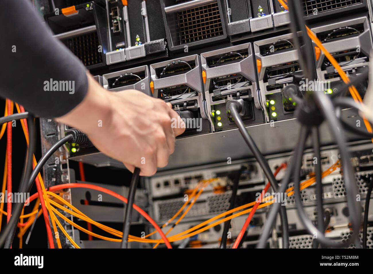 Tecnico maschio collegando il cavo di alimentazione nel pannello in corrispondenza del datacenter Foto Stock